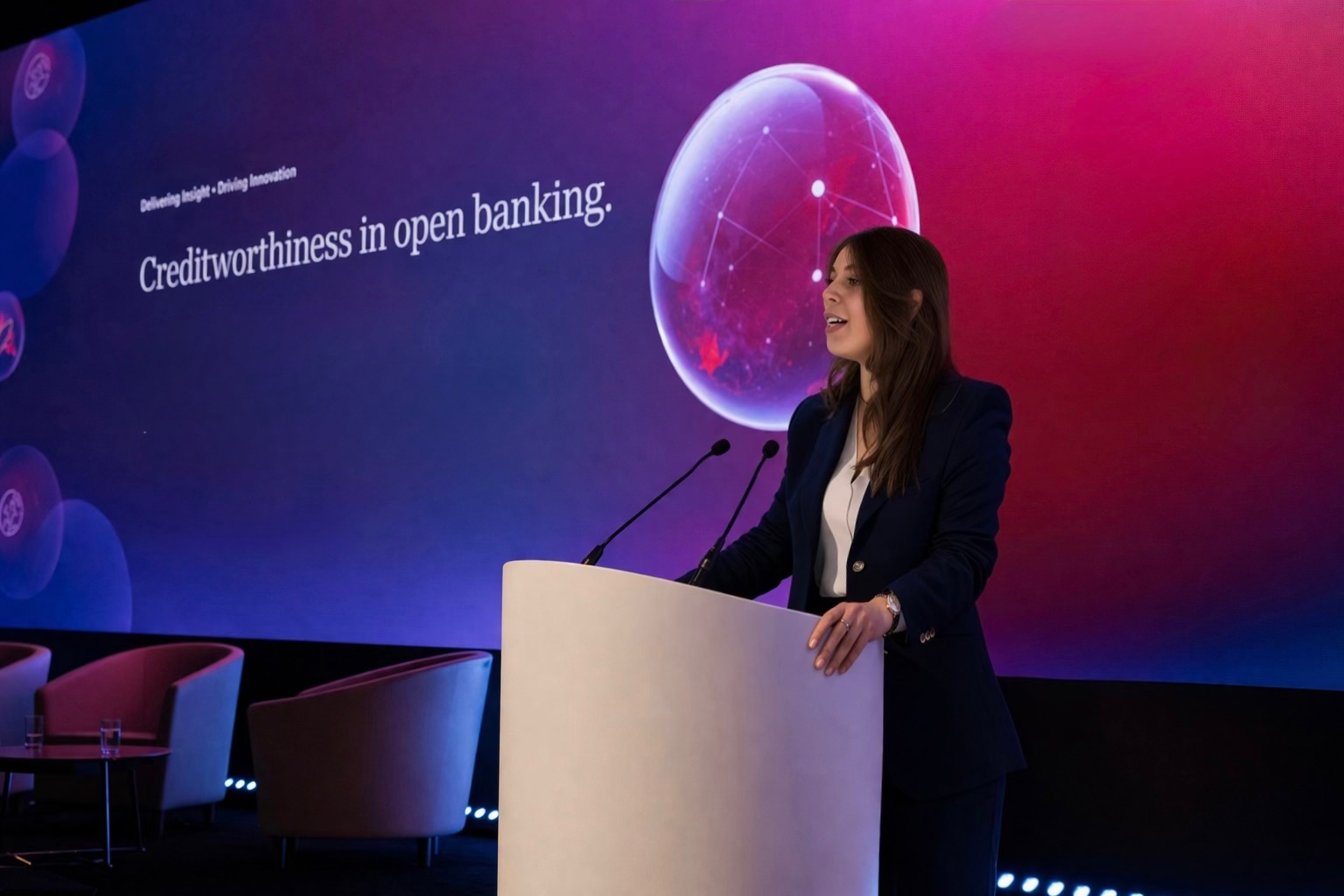 Natasha Cáceres speaking at a lectern during a conference on creditworthiness in open banking